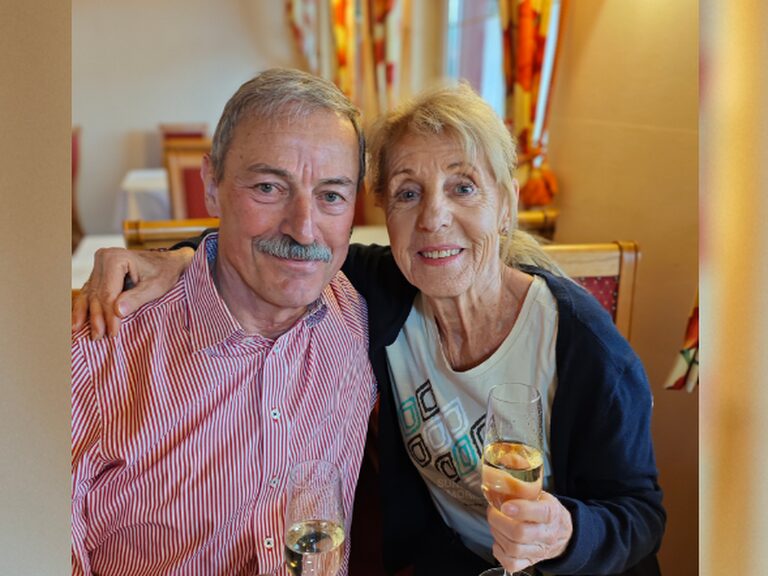 Paar sitzt eng umschlungen am Tisch, mit jeweils einem Glas Prosecco in der Hand
