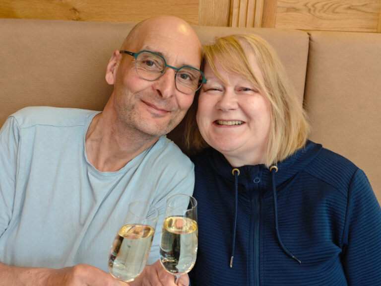 Paar sitzt am Tisch und stößt mit jeweils einem Glas Sekt auf den Geburtstag an
