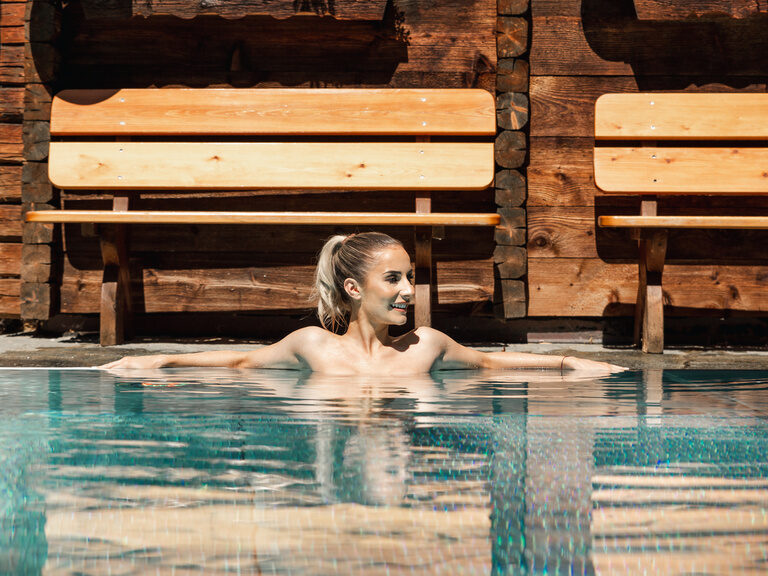 Frau lehnt sich an den Beckenrand des Aussenpools, die Sommersonne scheint