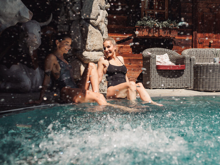 zwei Frauen auf dem Beckenrand des Außenpools sitzend und lachend