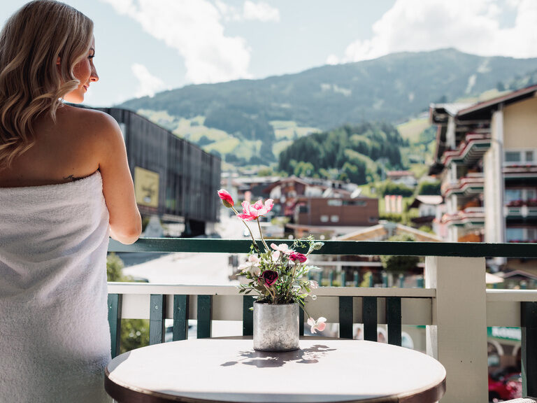Frau steht im Sommer in ein Handtuch gewickelt auf dem Balkon, mit Ausblick auf die Talstation der Spieljochbahn