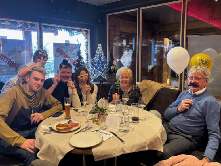 Mehrere Personen sitzen am Frühstückstisch und posieren mit lustigen Pappmasken