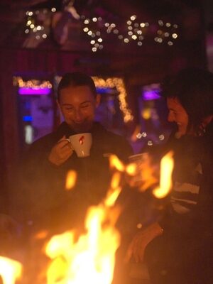 zwei Frauen stehen lachend mit einer Tasse Glühwein vor der Feuerschale des Kohlerhof-Winterzaubers