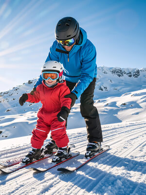 Man bringt dem Kind das Skifahren bei, es ist strahlender Sonnenschein und eine perfekt präparierte Piste zu sehen