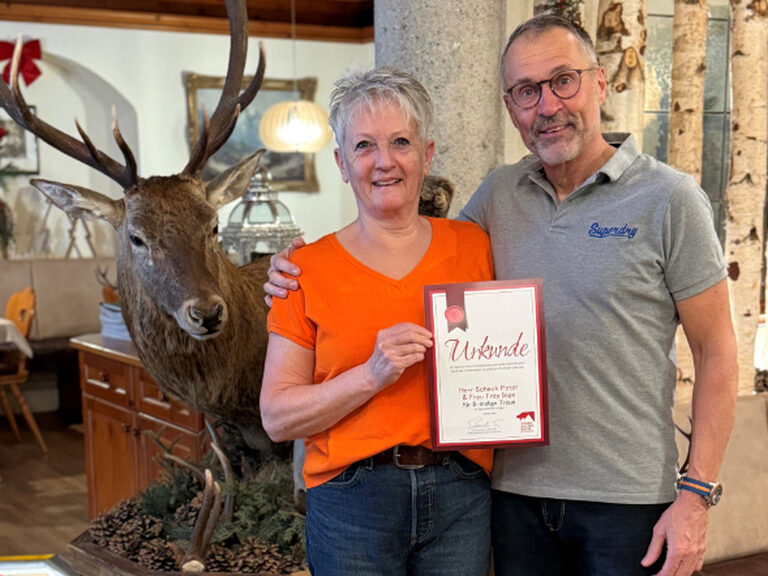 Paar posiert anlässlich Gästeehrung mit Urkunde und Geschenk