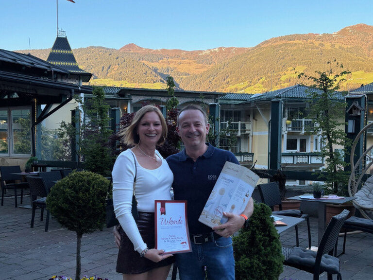 Paar steht auf der Gastterrasse des Kohlerhofs und posiert lächend mit der Ehrenurkunde