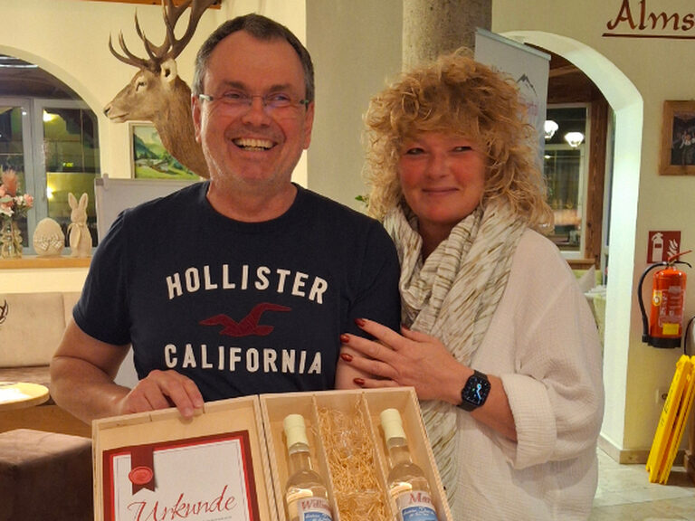 Paar hält Urkunde und Geschenk vom Hotel anlässlich Gästeehrung in den Händen und lächelt in die Kamera