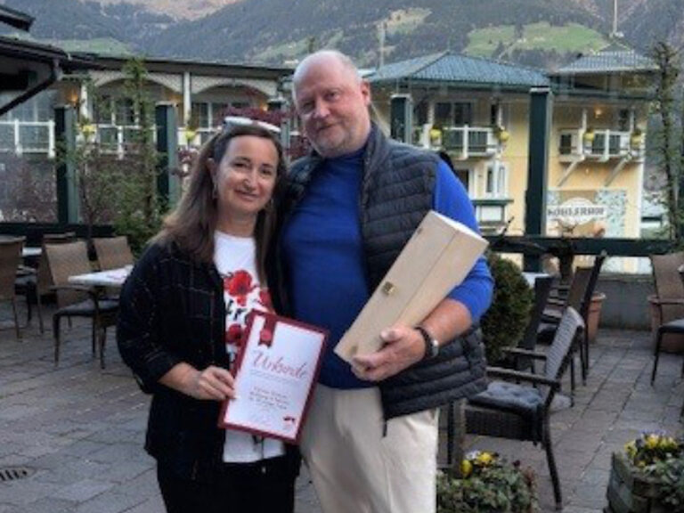 Paar steht auf der Gastterrasse des Kohlerhofs mit der Ehrenurkunde und dem Geschenk in den Händen
