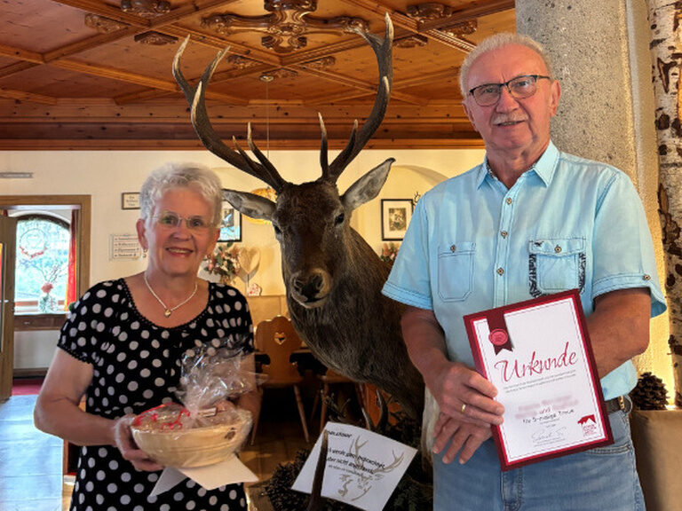 Paar posiert lächelnd mit Ehrenurkunde und Geschenk vom Hotel Kohlerhof