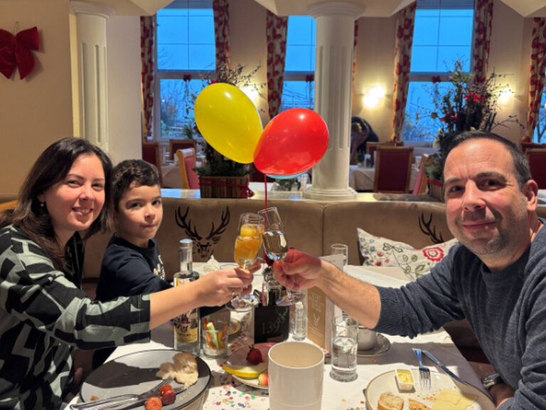 Familie sitzt am dekorierten Geburtstags-Frühstückstisch und prostet lächelnd in die Kamera