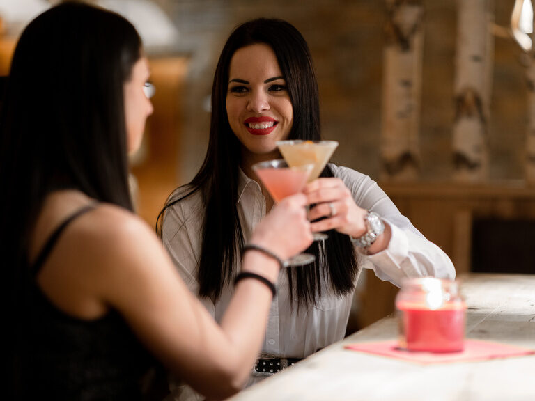 Zwei Frauen stoßen mit einem Getränk an