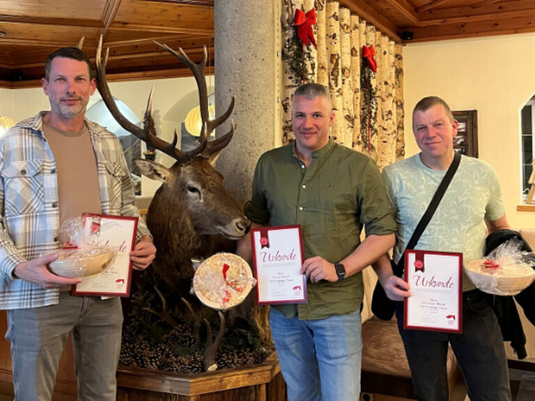 drei Männer stehen in der Hotellobby und zeigen jeweils ihre Gästeehrungsurkunde samt Geschenk in die Kamera