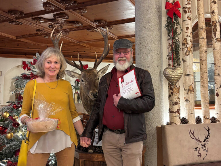 Paar lächelt fröhlich Hand in Hand - anlässlich der Stammgästeehrung - mit der Urkunde in die Kamera