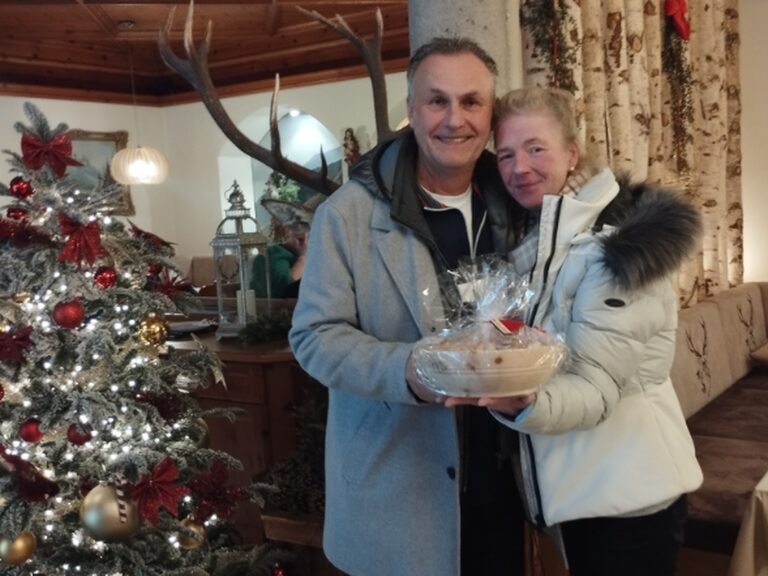 Paar posiert neben dem festlich geschmückten Weihnachtsbaum mit Geschenk vom Hotel anlässlich Ehrung