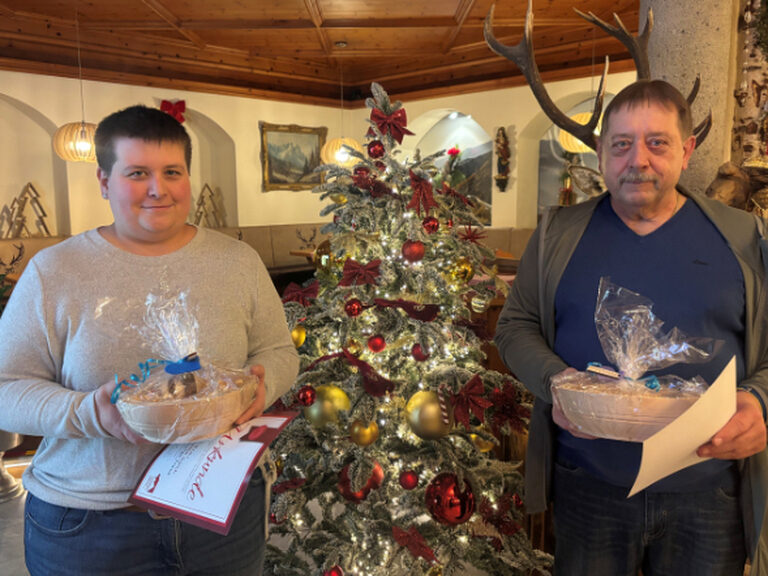 Paar posiert vor Weihnachtsbaum mit Urkunde und Geschenk anlässlich Gästeehrung