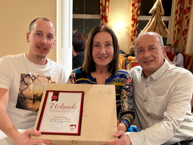 drei Personen posieren mit Urkunde anlässlich Gästeehrung