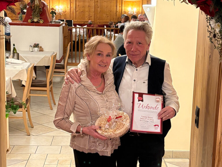 Paar posiert unter einem Blumenbogen mit Urkunde anlässlich Gästeehrung