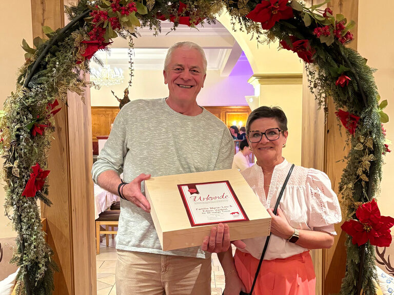 Paar posiert mit Urkunde anlässlich Gästeehrung unter dekoriertem Bogen