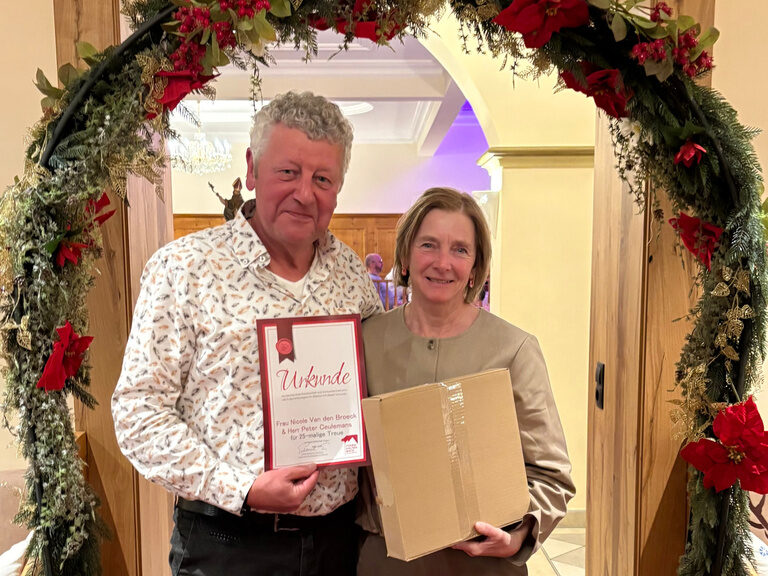 Paar posiert mit Urkunde anlässlich Gästeehrung unter dekoriertem Bogen