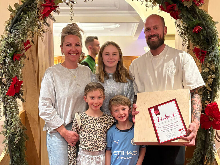 Familie posiert mit Urkunde anlässlich Gästeehrung unter dekoriertem Bogen