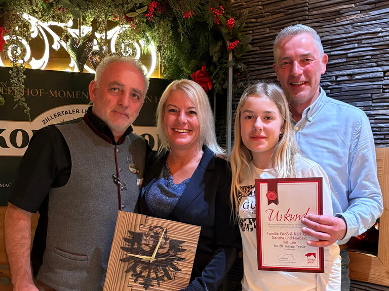 vier Personen posieren mit Urkunde anlässlich Gästeehrung unter dekoriertem Bogen