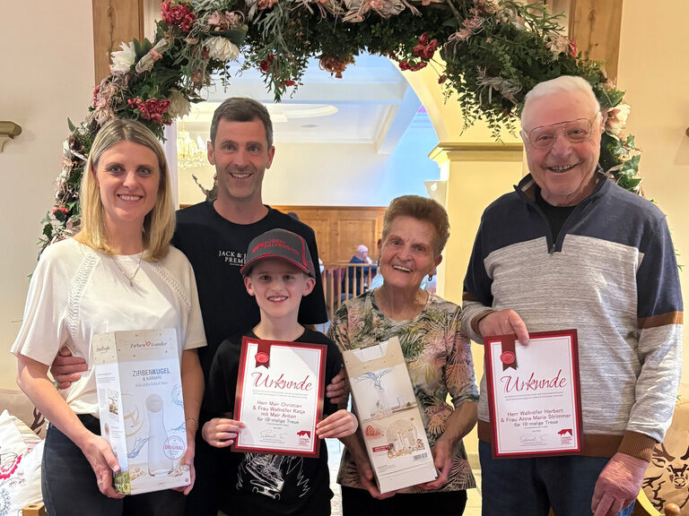 fünf Personen posieren anlässlich Gästeehrung unter dekoriertem Bogen