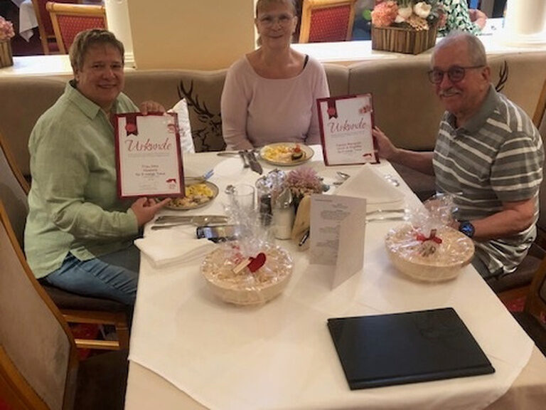 drei Personen sitzen am Tisch und posieren anlässlich Gästeehrung