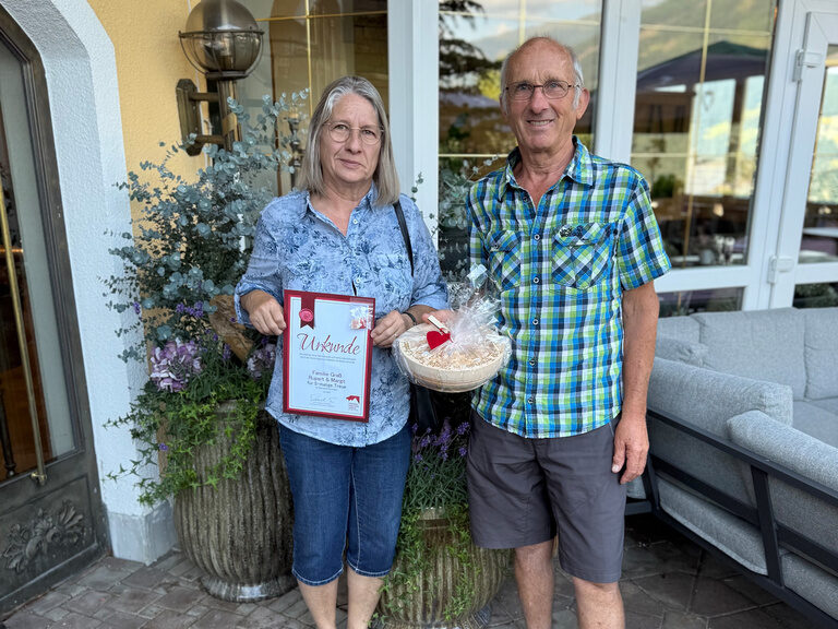 Paar posiert vor dem Hotel Kohlerhof mit Urkunde anlässlich Gästeehrung
