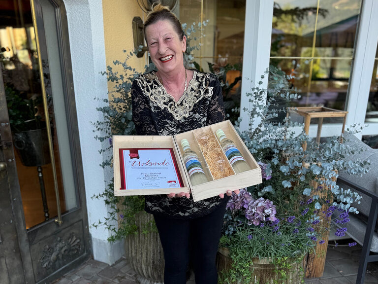 Frau posiert vor dem Hotel Kohlerhof mit Urkunde anlässlich Gästeehrung