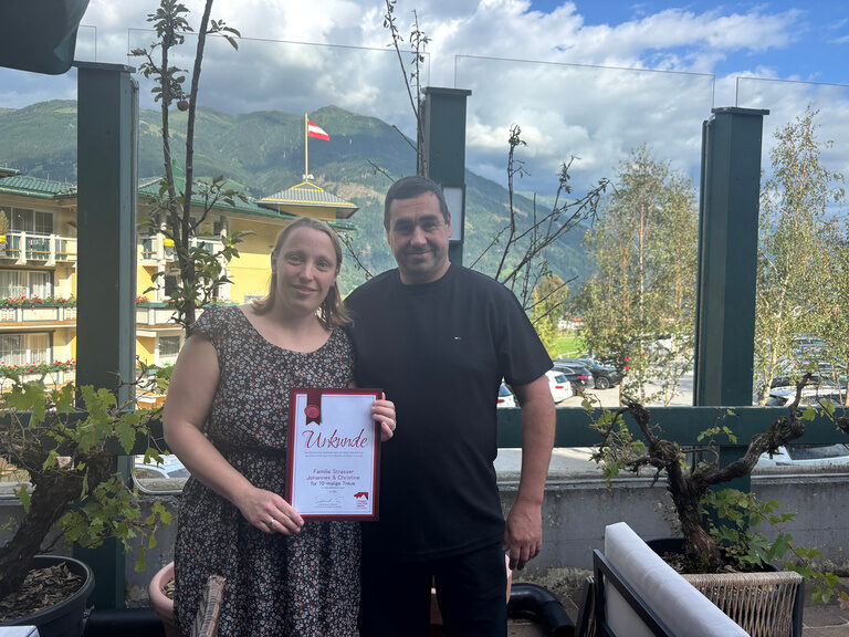 Paar posiert im Gastgarten mit Urkunde anlässlich Gästeehrung