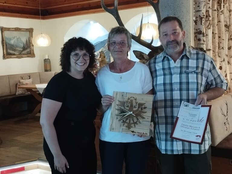 Paar posiert - gemeinsam mit Familienmitglied der Gastgeberfamilie - mit Urkunde anlässlich Gästeehrung