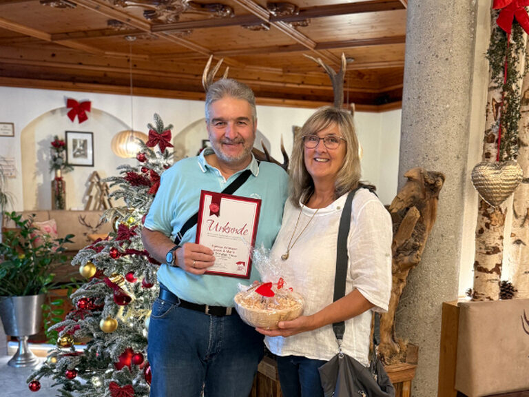 Paar posiert mit Urkunde anlässlich Gästeehrung, im Hintergrund ist weihnachtliche Deko zu sehen