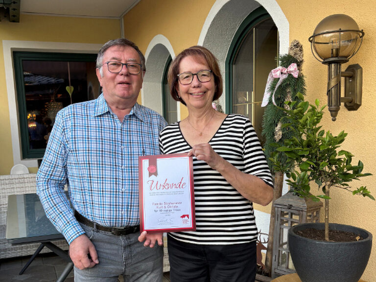 Paar posiert vor dem Kohlerhof mit Ehrenurkunde in der Hand
