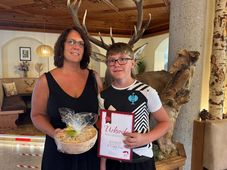 Frau und Kind halten Gästeehrungsurkunde und Geschenk vom Kohlerhof in der Hand und lächeln in die Kamera