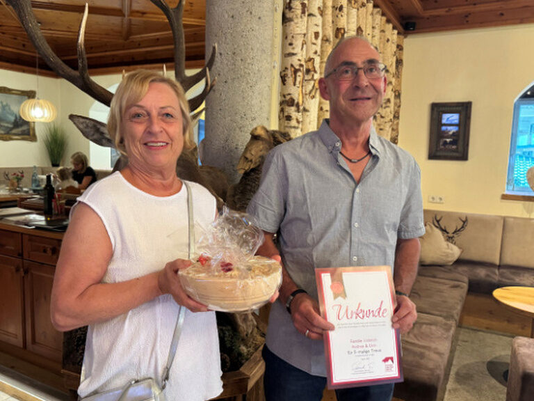 Paar posiert mit Urkunde und Geschenk vom Kohlerhof anlässlich Gästeehrung