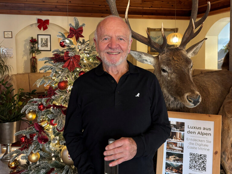 Mann posiert mit Geschenk anlässlich Geburtstag, dahinter ist der festlich geschmückte Weihnachtsbaum zu sehen