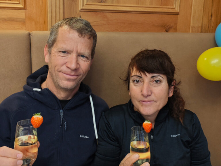 Paar posiert mit einem Glas Sekt anlässlich eines Geburstags, im Hintergrund sind ein blauer und ein gelber Luftballon zu sehen