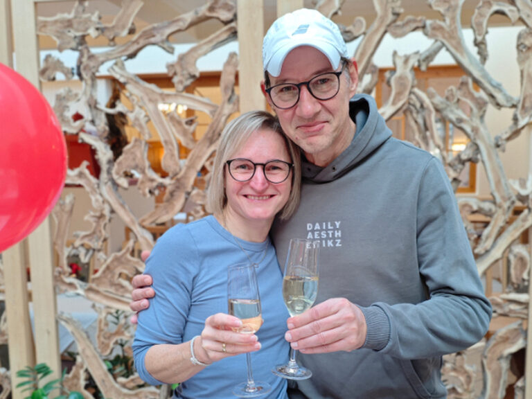 Paar lächelt eng umschlungen und hält anlässlich eines Geburtstags ein Glas Prosecco in der Hand