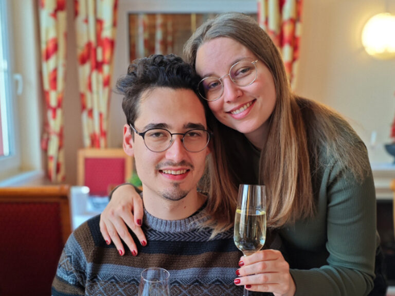 Aufgrund des Geburtstages des Mannes posiert ein Paar mit je einem Glas Sekt