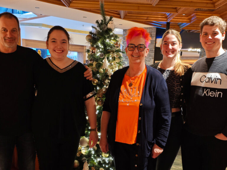 Familie posiert anlässlich Geburtstag vor dem weihnachtlich geschmückten Baum in der Hotel-Lobby