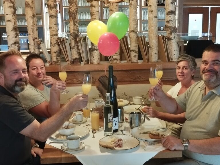 Familie sitzt am Frühstückstisch und stoßt anlässlich Geburtstag mit einem Sektglas an