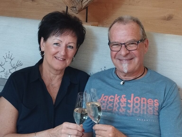 Paar sitzt am Tisch und stoßt anlässlich Geburtstag mit einem Glas Prosecco an