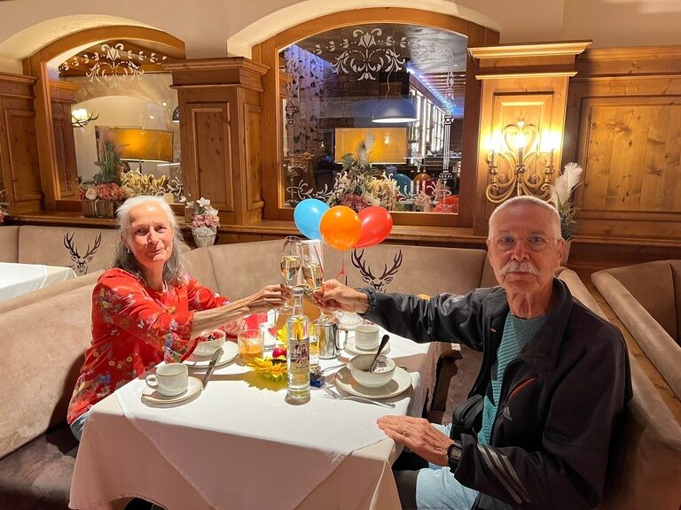 Paar sitzt am Frühstückstisch und stoßt anlässlich Geburtstag mit einem Sektglas an