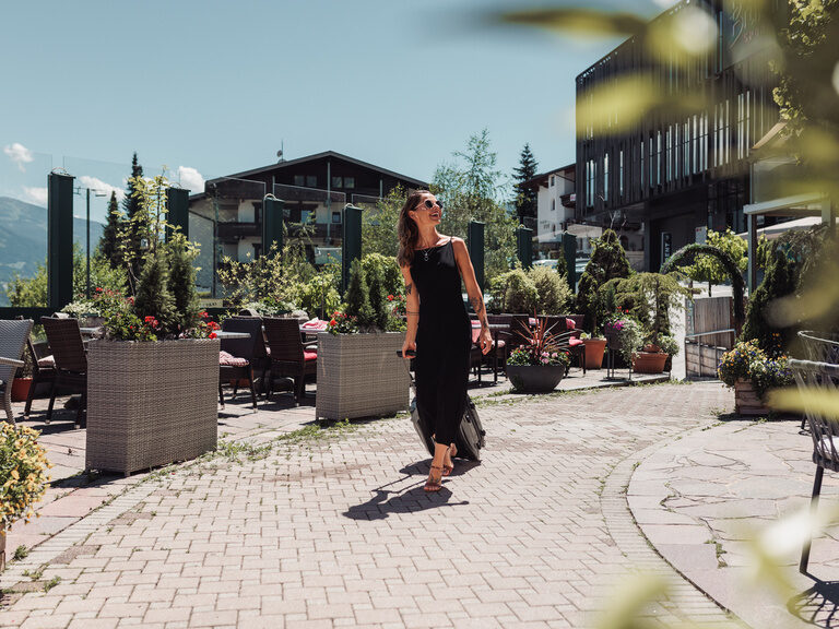 Frau in schwarzem Sommerkleid geht die Gastterrasse entlang