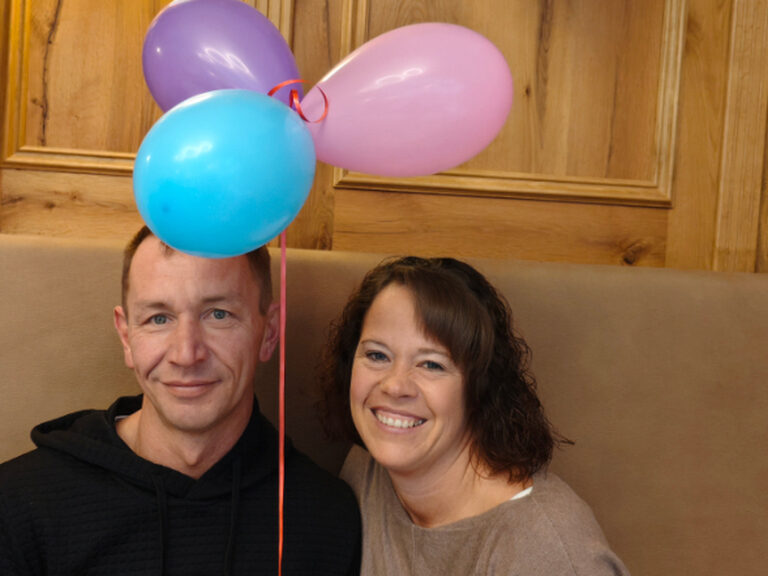 Paar posiert anlässlich eines Geburtstags, bunte Luftballone befinden sich ebenfalls auf dem Bild