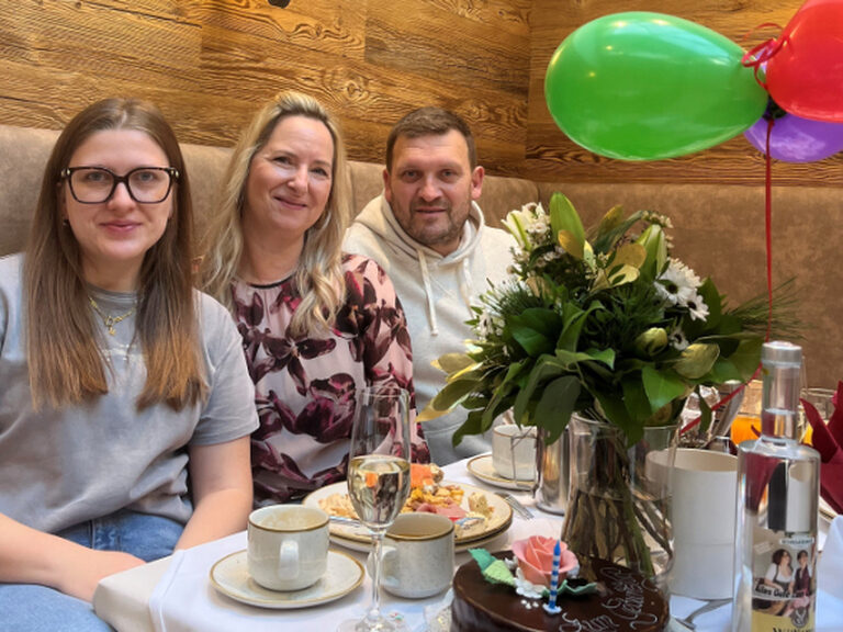 Familie sitzt am dekorierten Frühstückstisch, lächelt in die Kamera und feiert Geburtstag