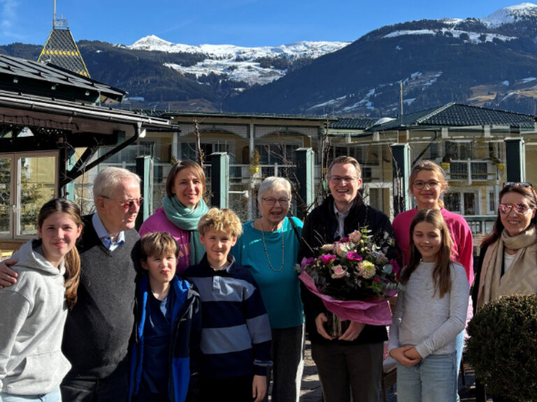 Eine Gruppe steht vor dem Hotel Kohlerhof, im Hintergrund ist strahlend blauer Himmel zu erkennen und das Geburtstagskind hält einen Strauß Blumen in den Händen
