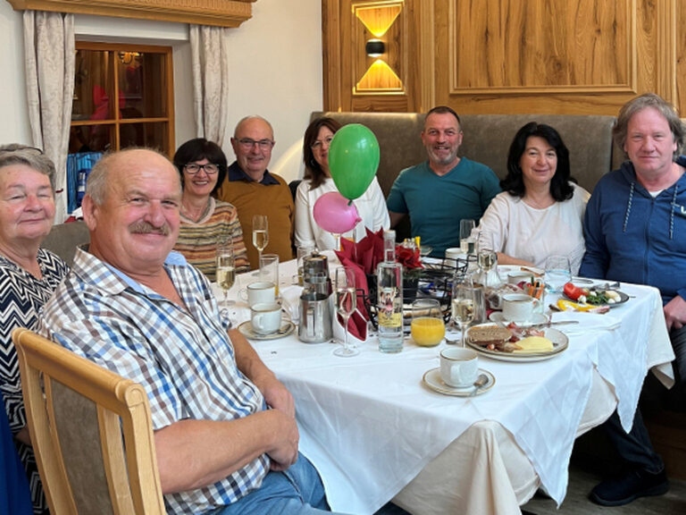 mehrere Gäste sitzen lächelnd am dekorierten Geburtstagstisch und feiern Geburtstag