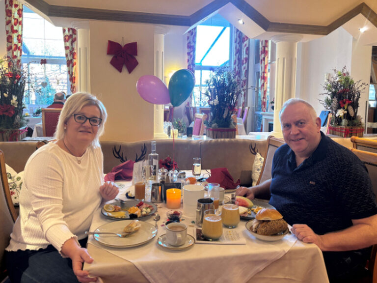 Paar sitzt am geschmückten Frühstückstisch und posiert anlässlich Geburtstag