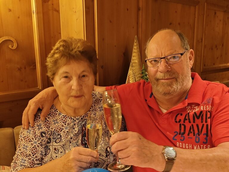 Paar sitzt mit Sektglas und Luftballonen am Tisch und posiert anlässlich Geburtstag